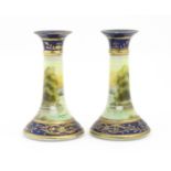 A pair of Noritake style candlesticks decorated with landscape scenes with swans, bordered with gilt