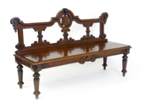 A Victorian mahogany bench, with a shaped top rail, carved terminals and an armorial shield to the