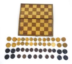 Toys: An early 20thC folding draughts / games board, containing a quantity of turned wooden counters