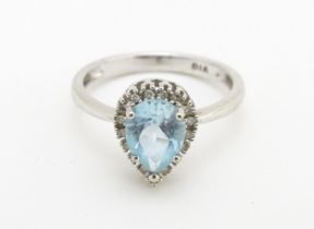 A 9ct white gold ring set with central blue topaz coloured stone bordered by diamonds. Ring size