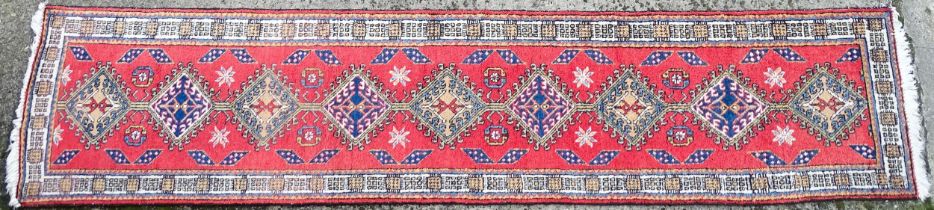 Carpet / Rug : A red ground runner decorated with central geometric motifs, floral details and