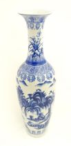 A tall Chinese blue and white vase with a flared rim decorated with a landscape scene with flowers