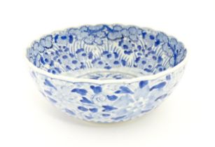 A Japanese blue and white bowl with scalloped edge decorated with a central vase of flowers bordered