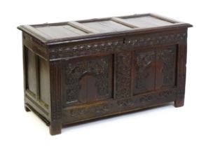 A late 17thC oak coffer with a three panel lid above a floral wave and scroll carved front, the
