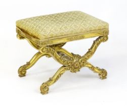 A late 19thC x-frame gilt stool, with a gesso and carved wood frame, the legs decorated with