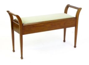An early 20thC mahogany piano stool flanked by carrying handles with an upholstered, hinged seat