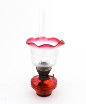 An early 20thC table oil lamp, the cranberry glass reservoir supporting a brass burner (marked '