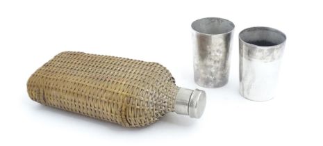 A 20thC wicker covered glass bottle. Together with two silver plate beakers by Mappin & Webb. Bottle