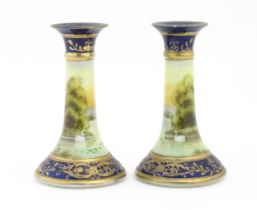 A pair of Noritake style candlesticks decorated with landscape scenes with swans, bordered with gilt