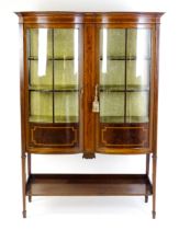 An early 20thC mahogany display cabinet with a double bowed front and satinwood crossbanding to