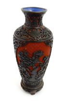 A Chinese cinnabar lacquer style vase with floral and foliate decoration, on a carved hardwood