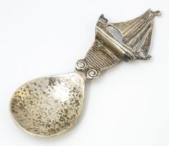 An Arts & Crafts style silver caddy spoon with hammered bowl, the handle surmounted by a sailing