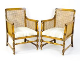 A pair of 20thC bergère armchairs with caned backrests and sides, drop in seats and raised on turned