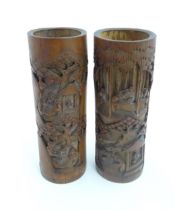 A pair of Oriental carved bamboo vases of cylindrical form decorated with figures in a wooded