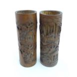 A pair of Oriental carved bamboo vases of cylindrical form decorated with figures in a wooded