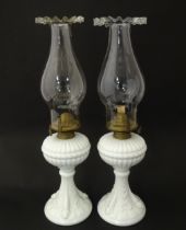 A pair of 19thC table oil lamps, the milk glass column bases with integral reservoirs, decorated