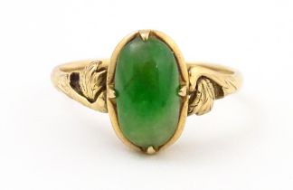 A 14ct gold ring set with green jade style cabochon with scroll detail to shoulders. Ring size