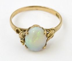 A 14ct gold ring set with opal cabochon with foliate scroll detail to shoulders. Ring size approx. M