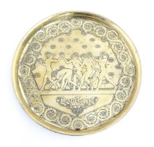 A 20thC German brass charger decorated with Pan playing the flute with dancing nymphs, titled Der