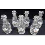 A SET OF SIX SMALL CUT GLASS DECANTERS, WITH PORCELAIN LABELS