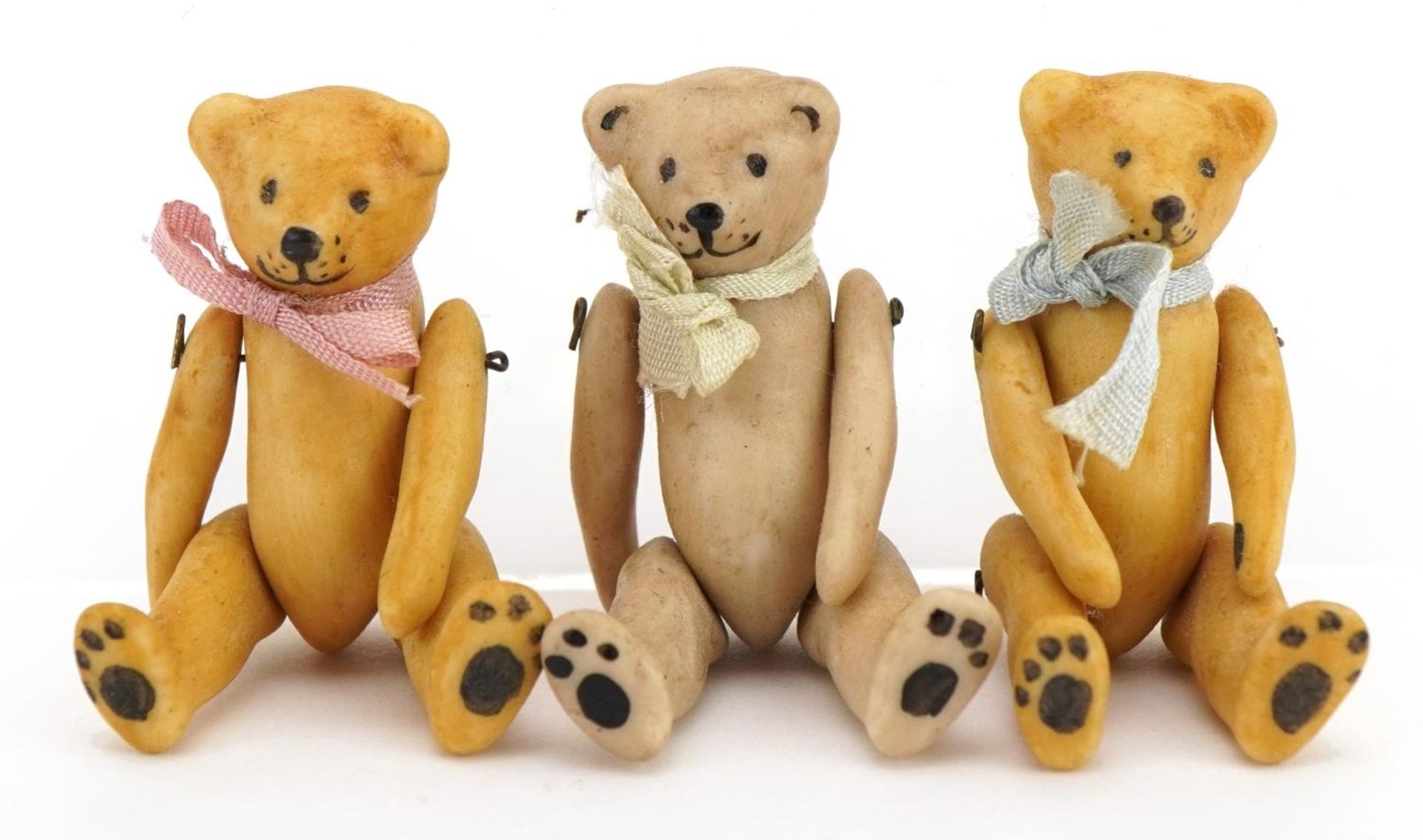 Three miniature bisque teddy bears with jointed limbs in the manner of Hertwig, each 3.7cm high