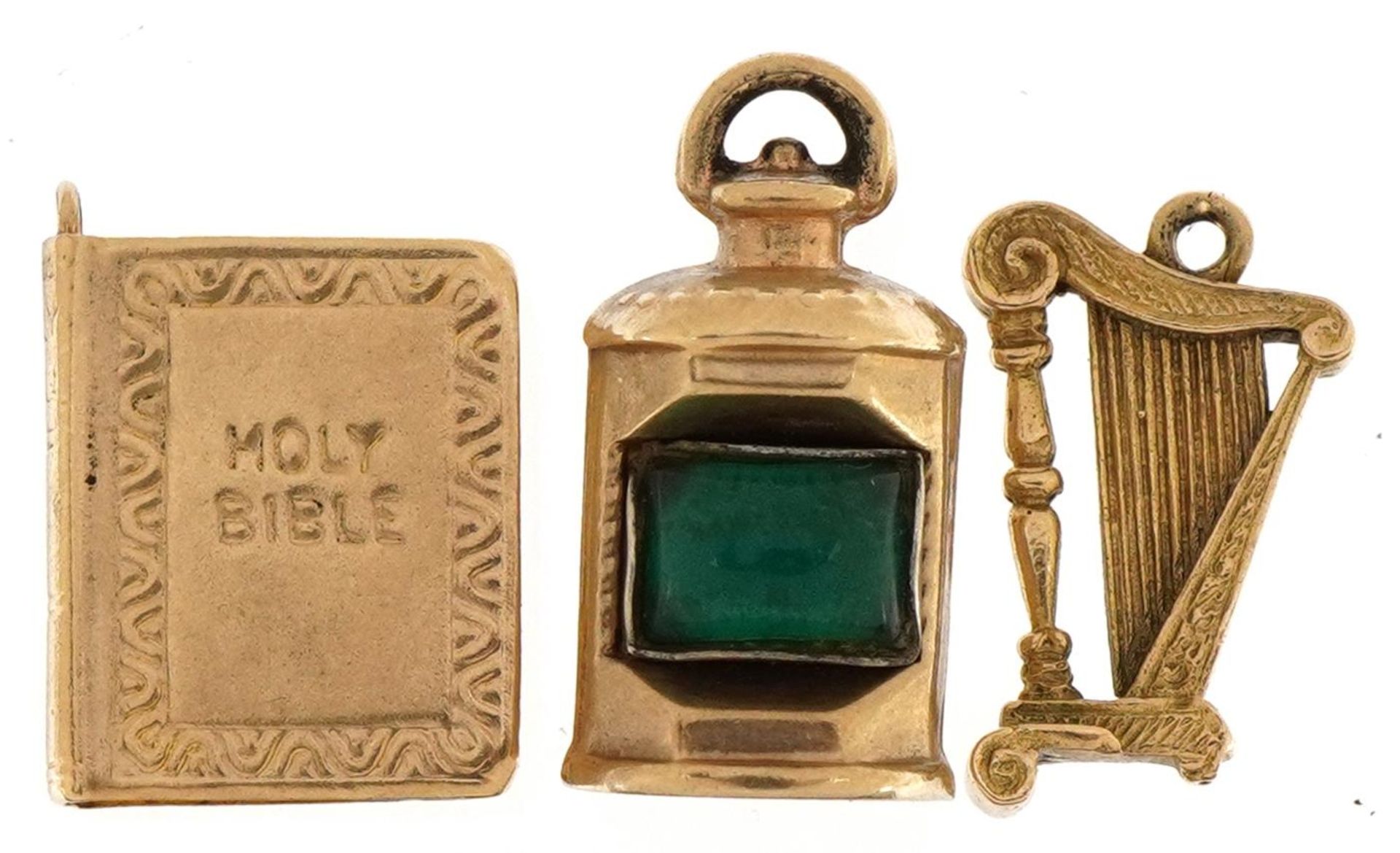 Three 9ct gold charms comprising bible, harp and lantern set with a green stone, the largest 1.9cm