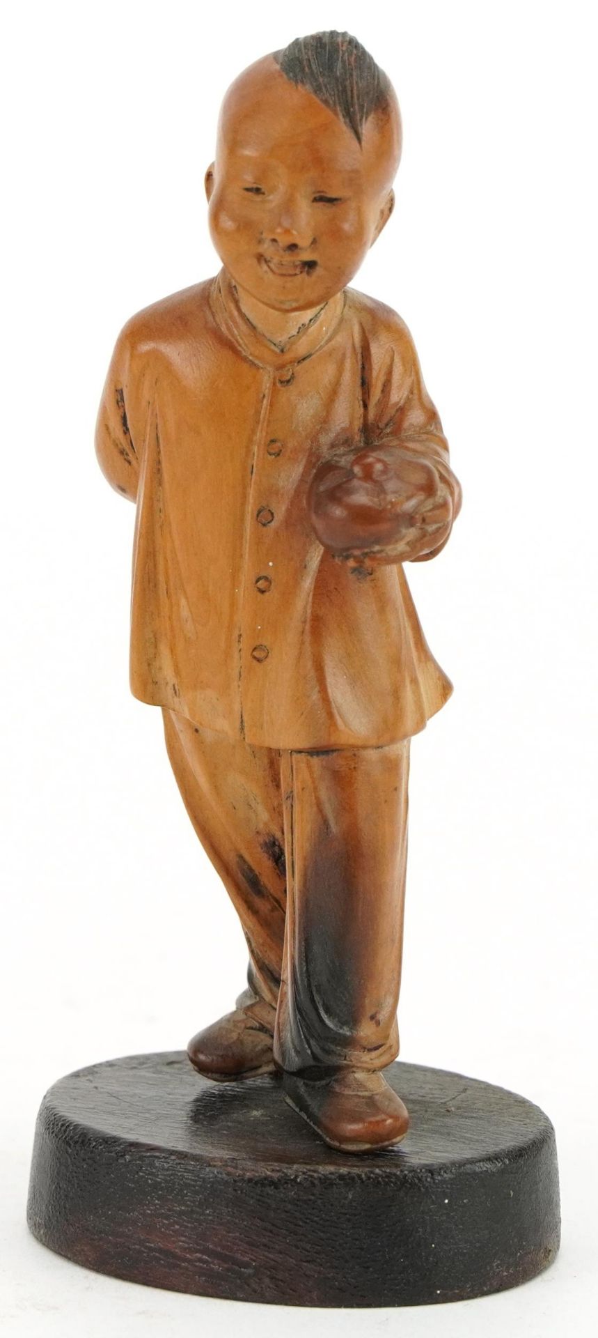 Chinese boxwood carving of a young boy holding a fruit, raised on an oval base, 11cm high
