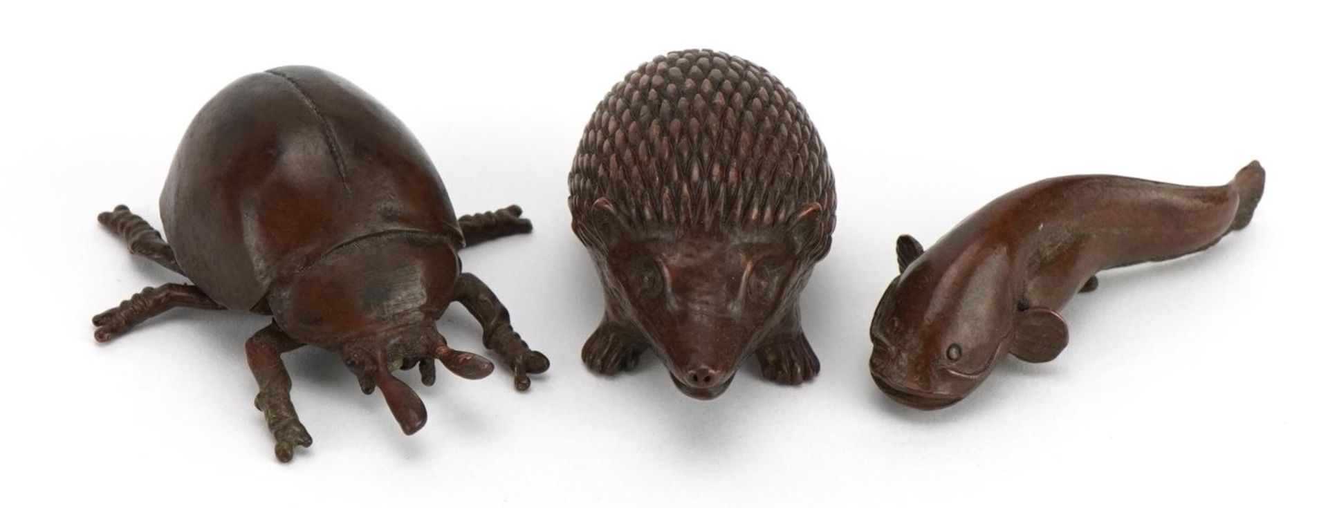 Three Japanese patinated bronze animals comprising hedgehog, beetle and fish, each with impressed