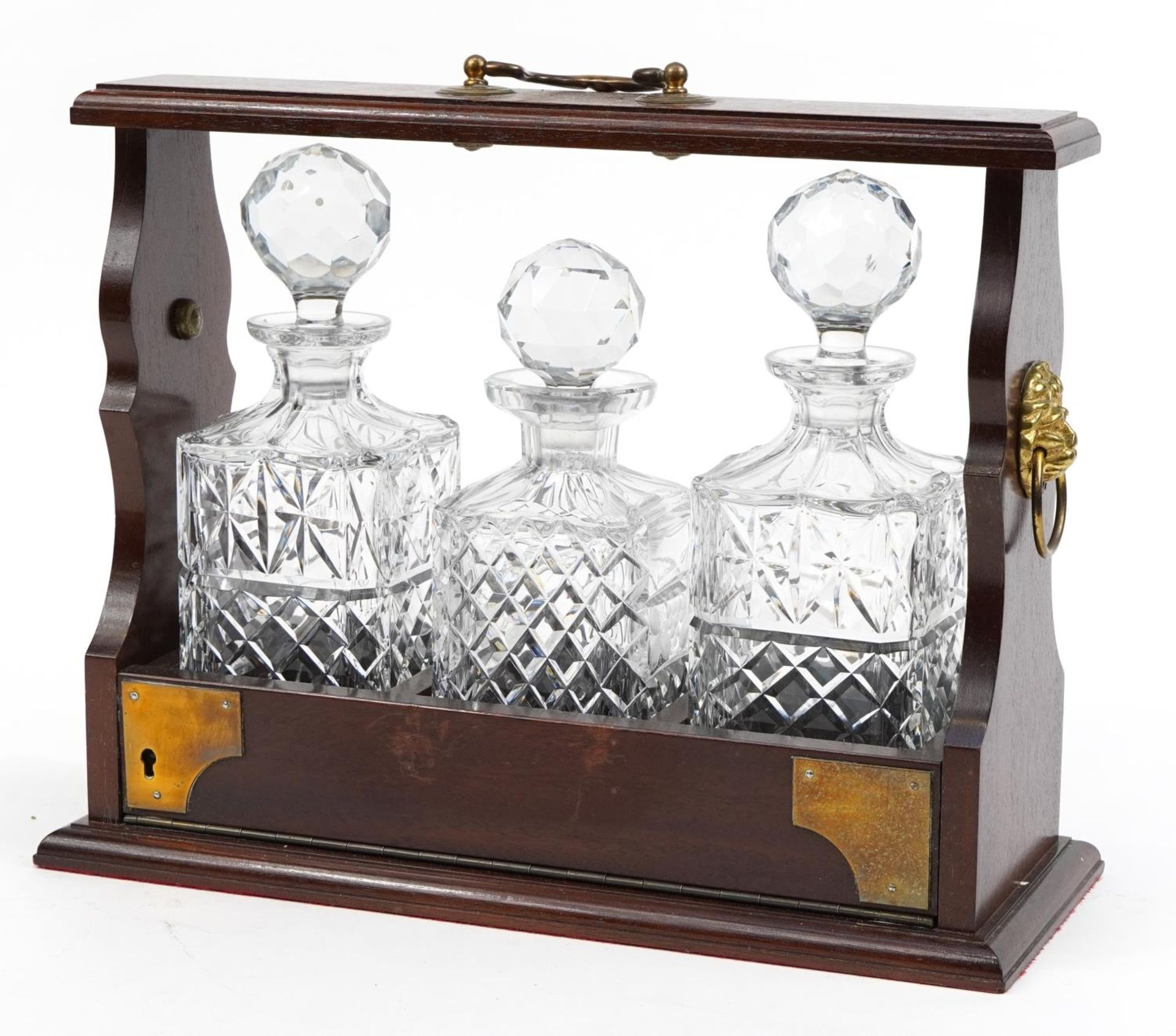 Mahogany three bottle tantalus with brass ring turned lion head handles and three glass decanters,