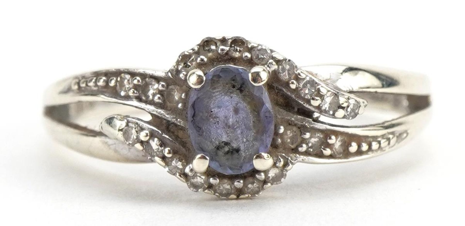 9ct white gold purple stone and diamond crossover ring, the band stamped 0.10 carat, size L, 2.1g