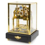 Congreve style rolling ball clock housed under a glazed brass display case with ebonised base,