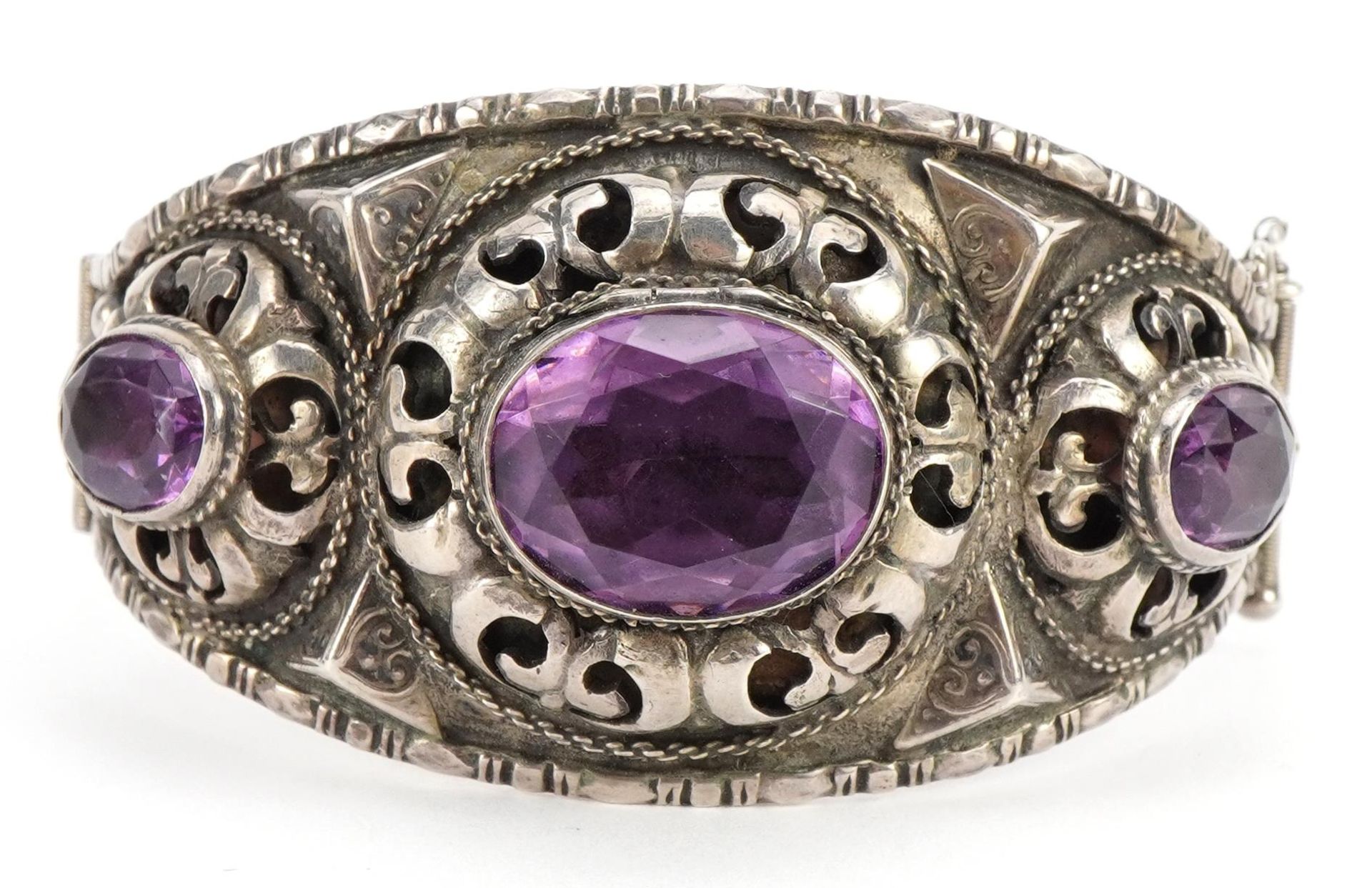 Antique unmarked silver and amethyst hinged bangle with pierced and embossed decoration, 6.7cm wide