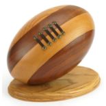 Wooden sculpture of an American football raised on an oval plinth base, 27cm wide x 24cm high