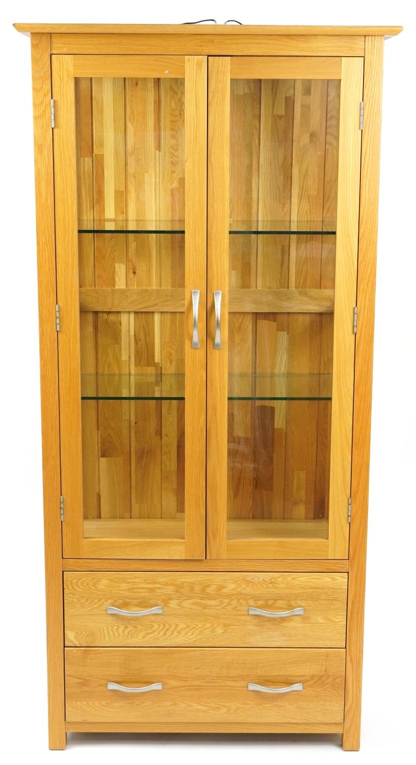 Contemporary light oak illuminated display cabinet with a pair of glazed doors, two glass shelves