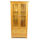 Contemporary light oak illuminated display cabinet with a pair of glazed doors, two glass shelves