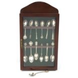 Thirteen silver sporting and souvenir teaspoons housed in a mahogany display case, the largest 12.