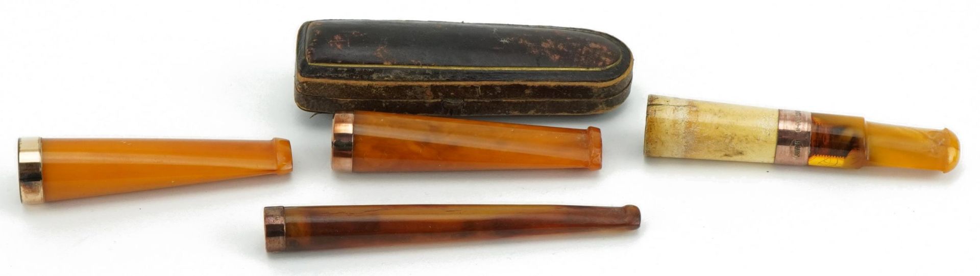 Four late 19th/early 20th century amber and amber coloured cigarette holders with 9ct gold and