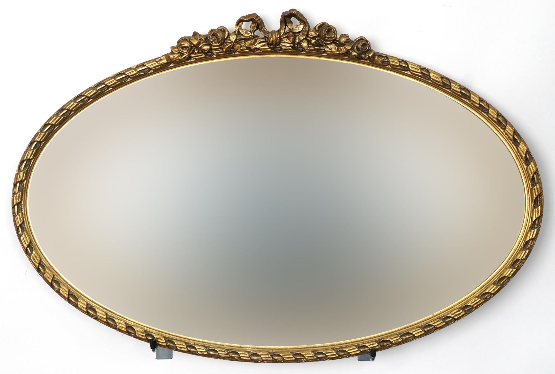 Oval gilt framed wall hanging mirror with bow crest and bevelled glass, 73cm x 48cm