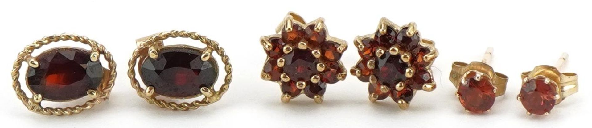 Three pairs of 9ct gold garnet earrings comprising solitaire studs and flower head clusters, the