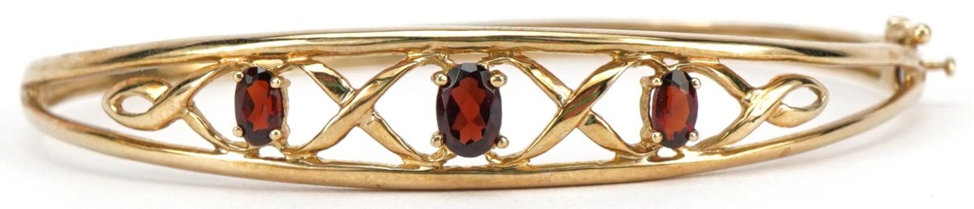 9ct gold garnet Celtic design hinged bangle, the largest garnet approximately 6.0mm x 4.0mm, 6.3cm