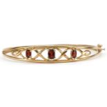 9ct gold garnet Celtic design hinged bangle, the largest garnet approximately 6.0mm x 4.0mm, 6.3cm