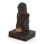 Tribal interest pottery figure of a crouched nude male raised on a wooden square block base, 13cm