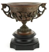 Bronzed Campana urn decorated in relief with flowers and twin handles, raised on a black slate