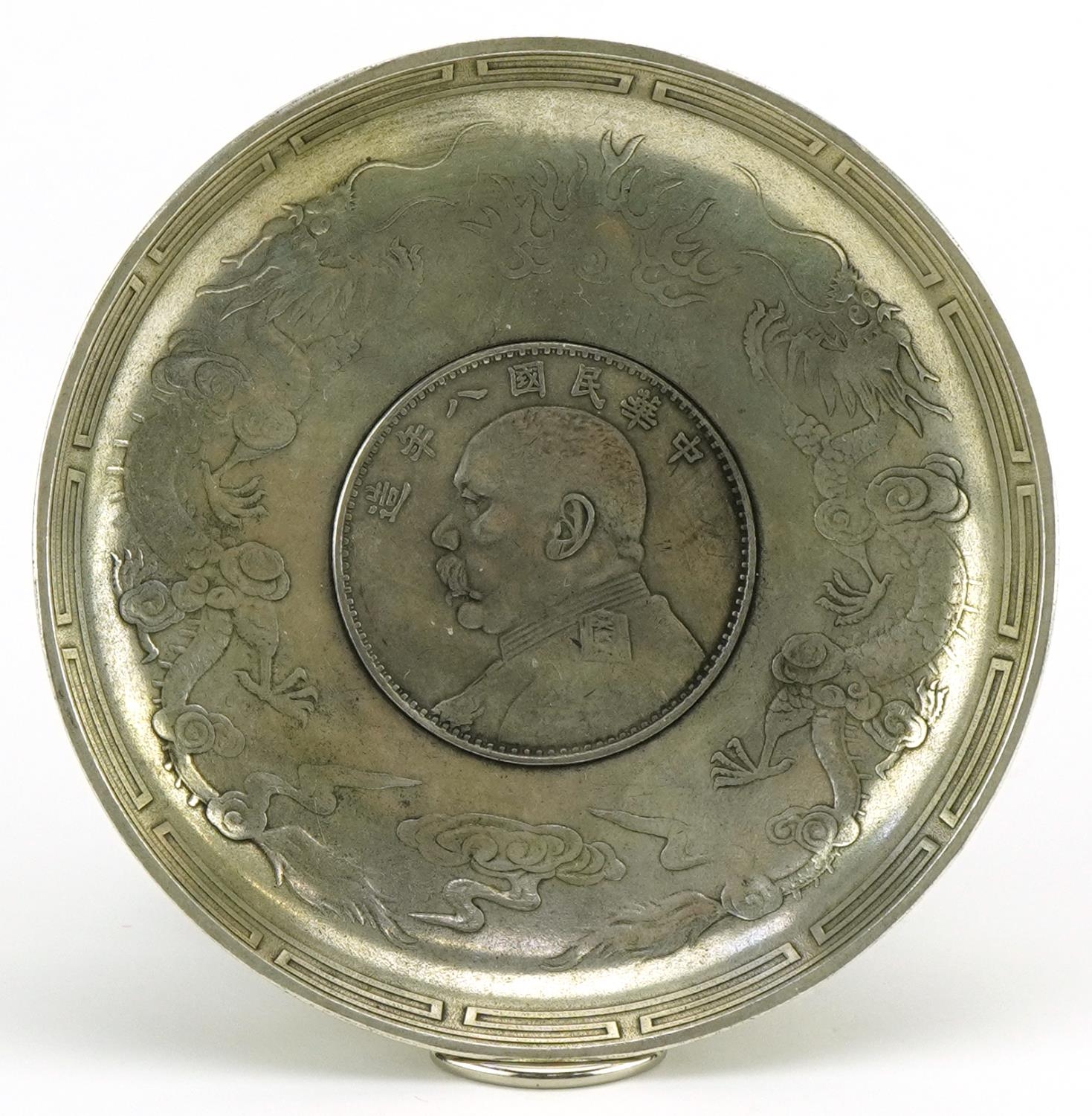 Chinese white metal dragon dish inset with a coin, 9.5cm in diameter : For further information on