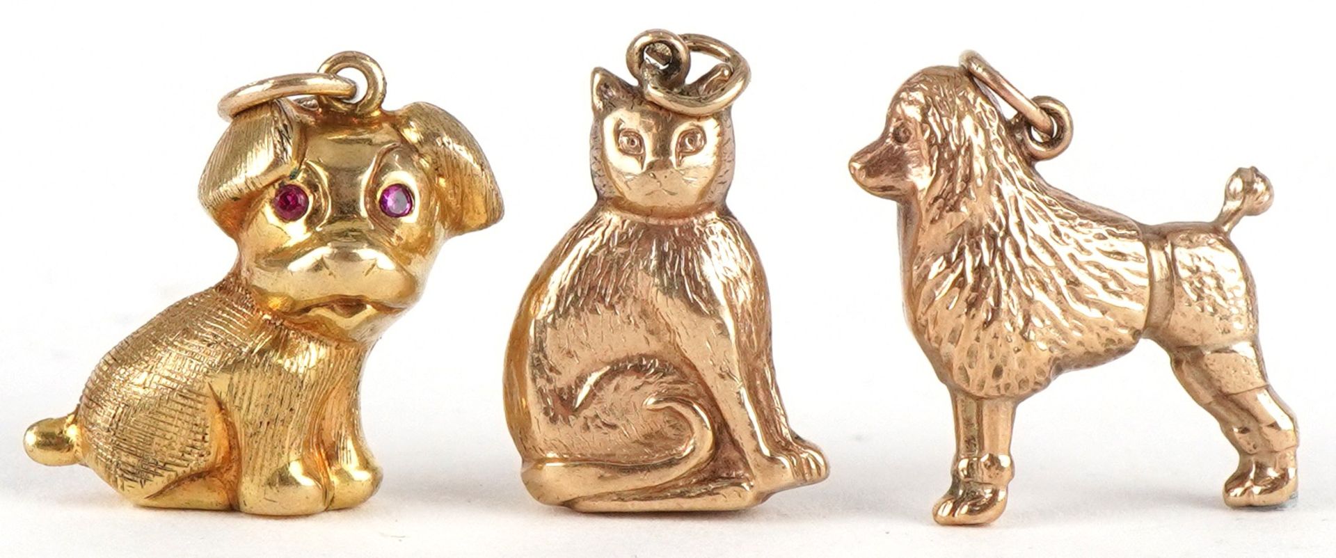 Three 9ct gold animal charms comprising Poodle, seated cat and seated dog with ruby eyes, the