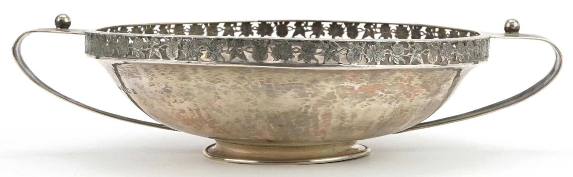 A E Jones, Arts & Crafts planished footed bowl with twin handles and pierced floral border,