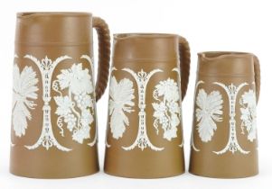Graduated set of three 19th century Jasperware style jugs decorated in relief with berries and