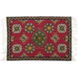 Rectangular Moroccan rug having an all over repeat flower head design onto a red ground, 88cm x 57cm