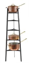 Three Victorian copper and brass saucepans housed in a tapering wrought cast iron rack : For further