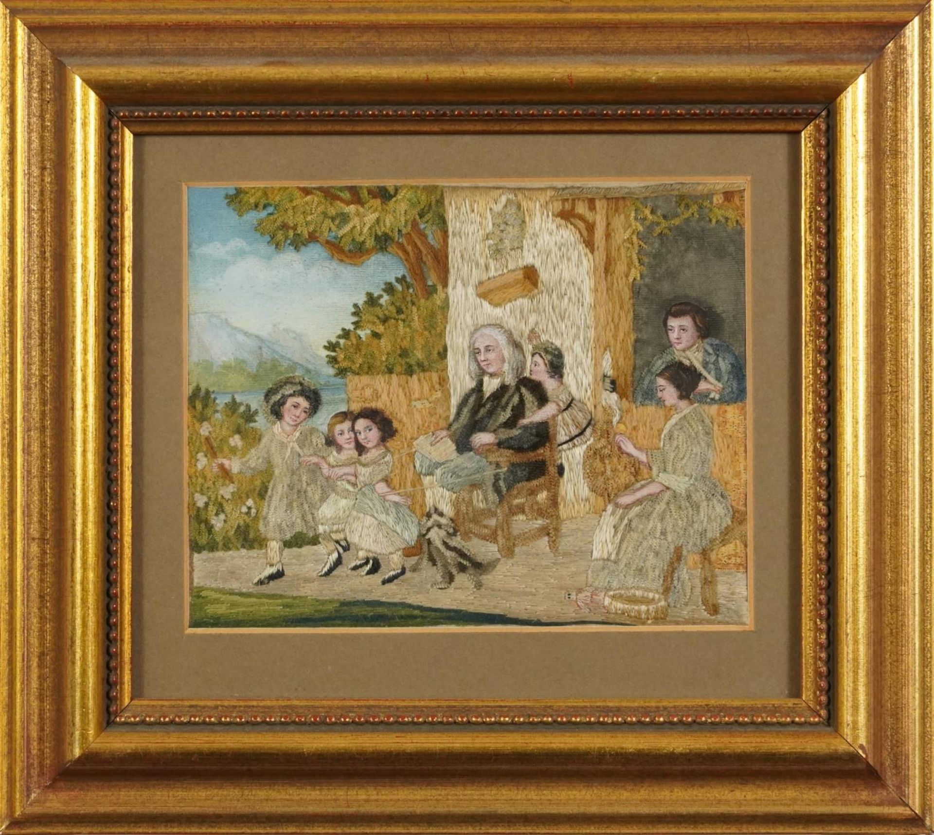 Antique silk work picture hand painted and worked with a family playing before a landscape, - Image 2 of 3